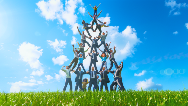 About the post: Images are AI-created. Prompt: Photorealistic image of diverse bankers of various genders and ethnicities wearing business attire, forming a multi-level acrobatic human pyramid, in a serene lush green field on a bright sunny day with a clear blue sky, smiling faces, sense of unity and happiness, overhead angle, faces uplifted, a humorous scene. Tool: Midjourney.